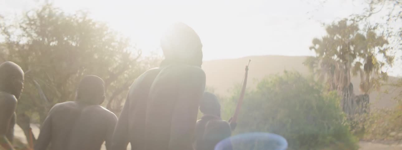 A group of tribal men hunt together with bows on a grassland during the day