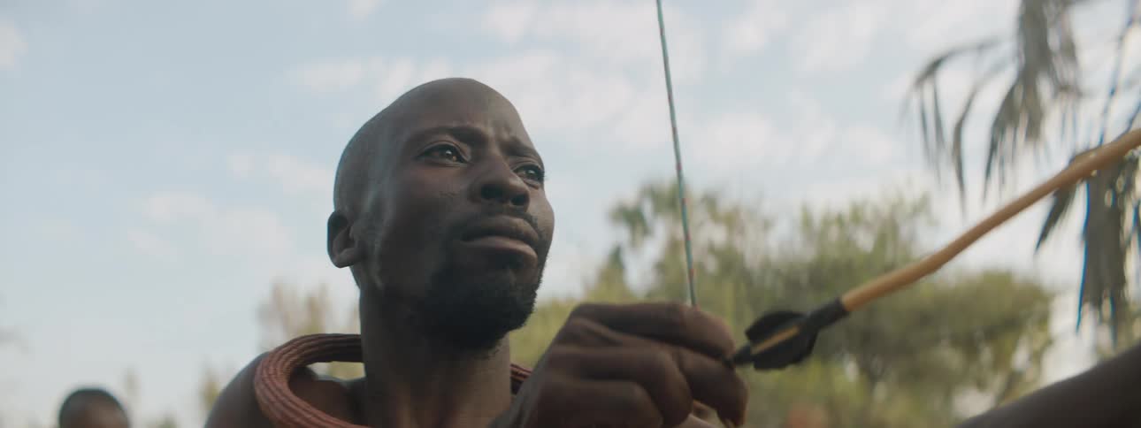 A man aiming a bow and arrow with trees the sky and clouds in the background