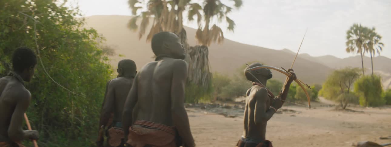 Members of a tribe walk across the land with bows and arrows ready as they hunt