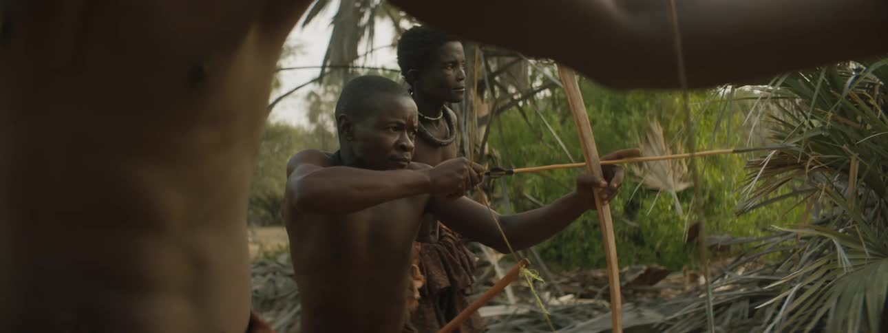 Members of a tribe in a rural village practice shooting with a bow and arrow