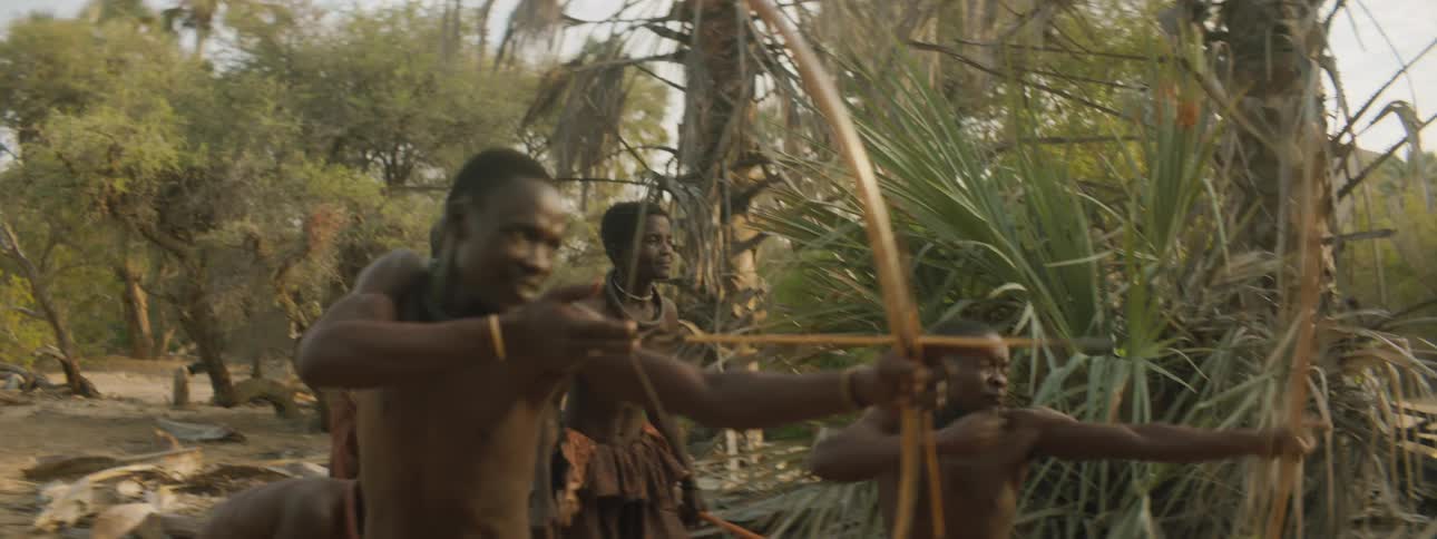 Two natives with bows and arrows looking for a target and shooting at it while other natives watch