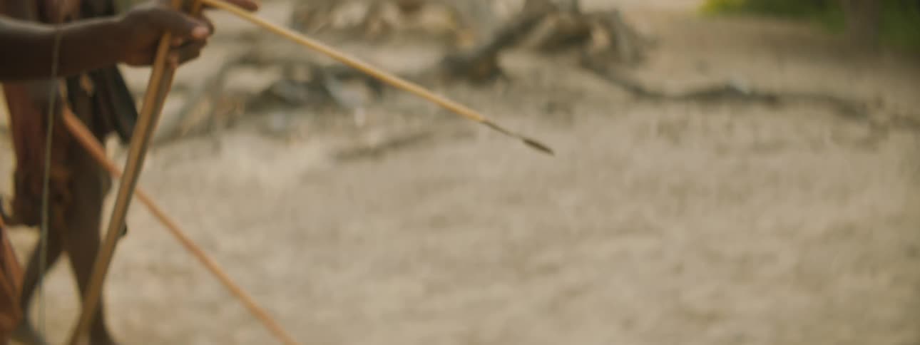 A person walking with a bow and arrow with trees the sky and clouds in the background