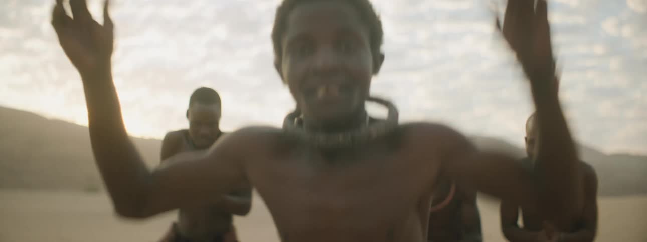A young boy walks in front of his tribe and does a tribal dance as they all clap