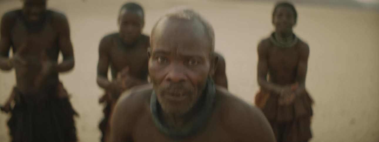 Members of a tribe dance and clap in a desert