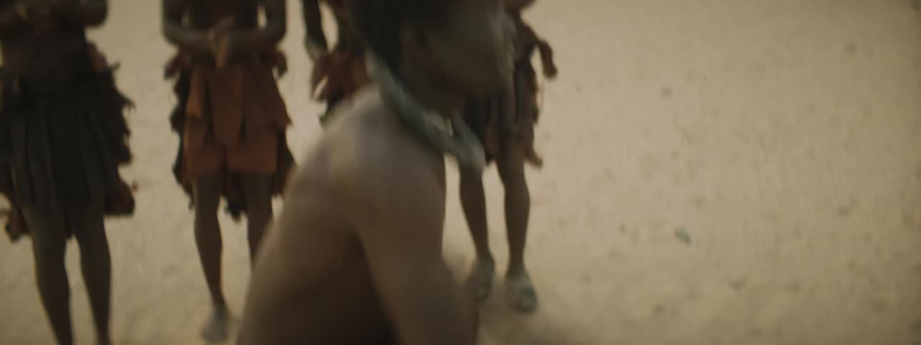 A young boy danes in the desert as members of his tribe clap along