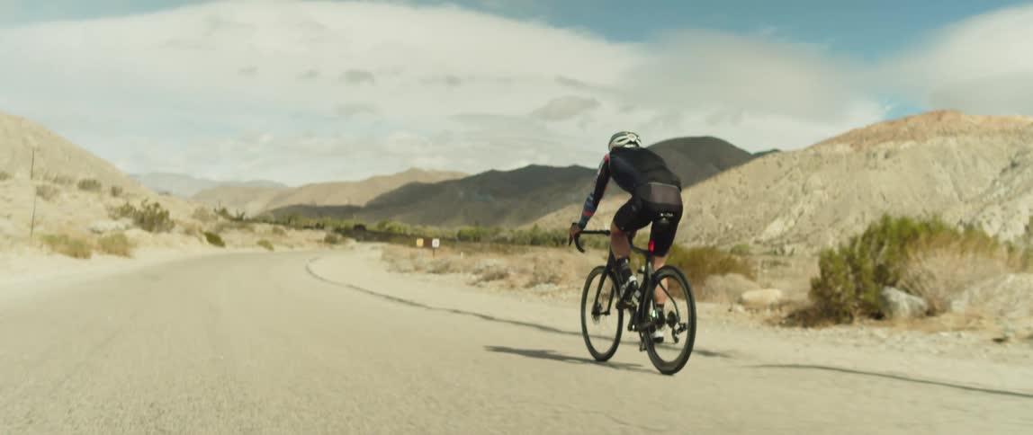 A cyclist rides a bicycle along a road through an arid mountainous countryside during the day