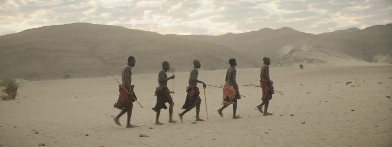 Five men in a tribe walk across the desert