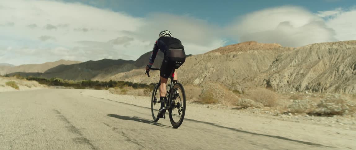 A man wearing a bicycle helmet is riding a bike on a dirt road near mountains