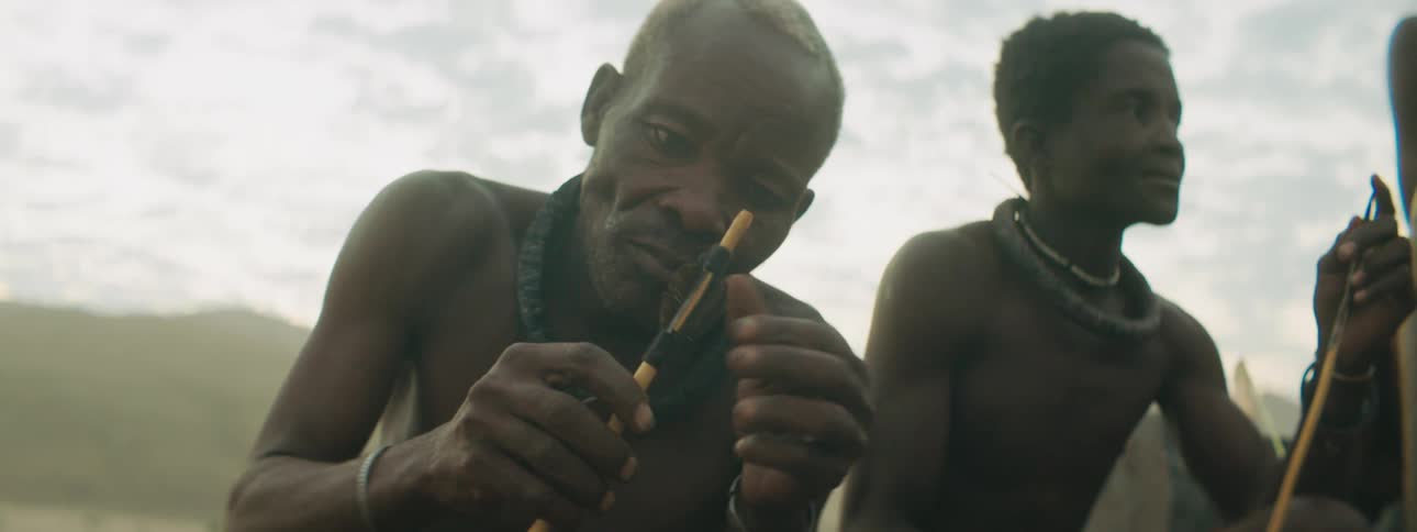 People in a tribe sit outside and look at arrows