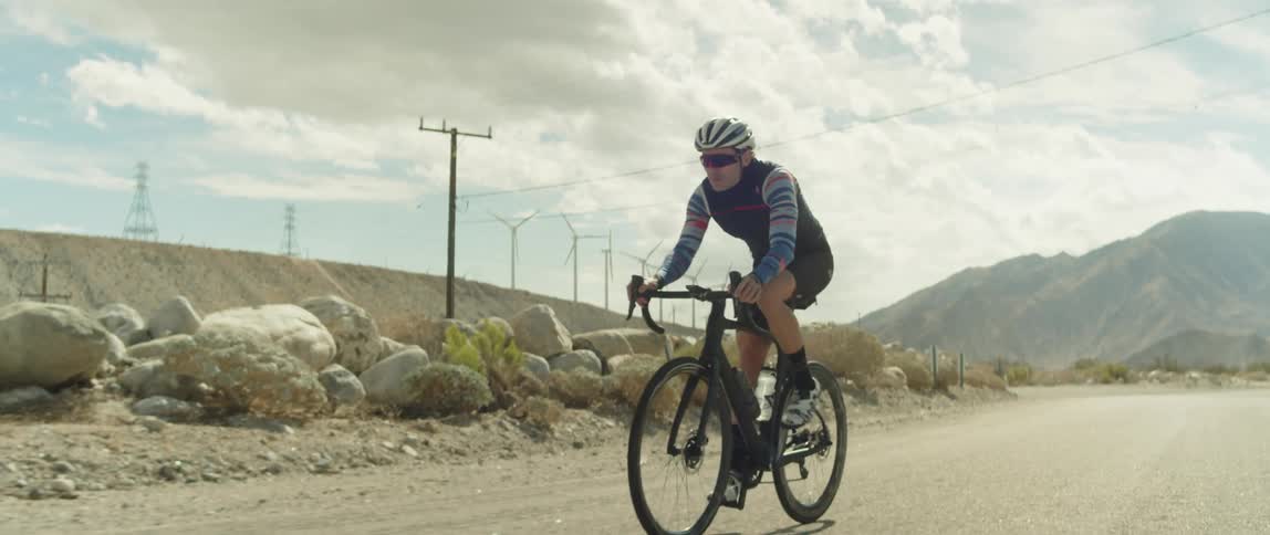 Man wearing a helmet rides a bicycle on a road in the desert close to the mountains