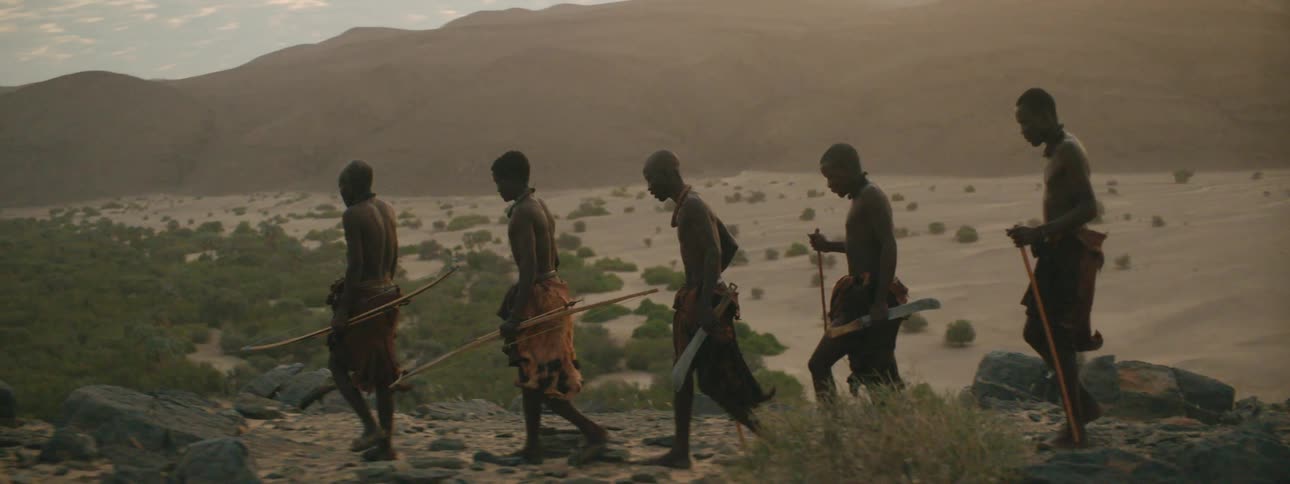 Men walking with sticks with a mountain range the sky and clouds in the background