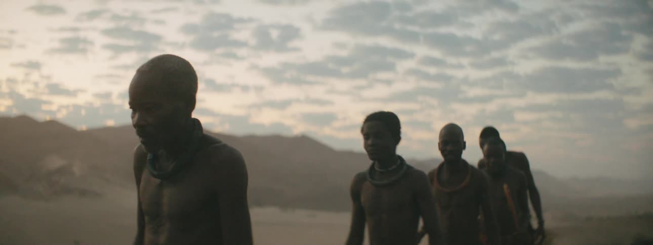 Men walking in a line with a mountain range the sky and clouds in the background