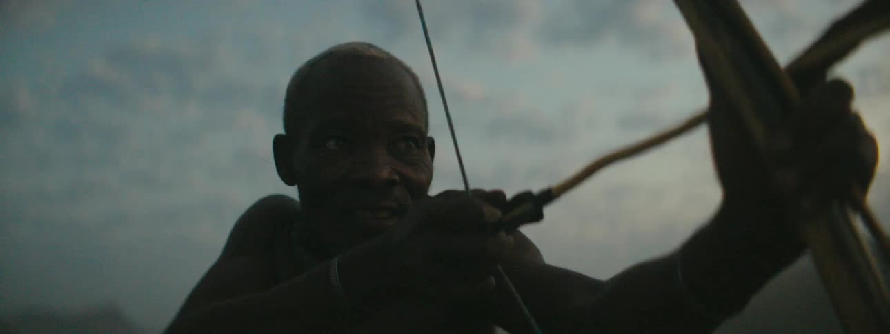 Man stands outdoors aiming arrow on wooden bow
