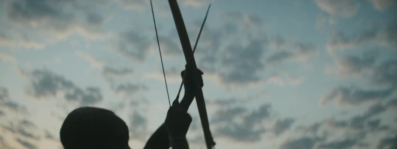A silhouette of a man with a bow and arrow with the sky and clouds above