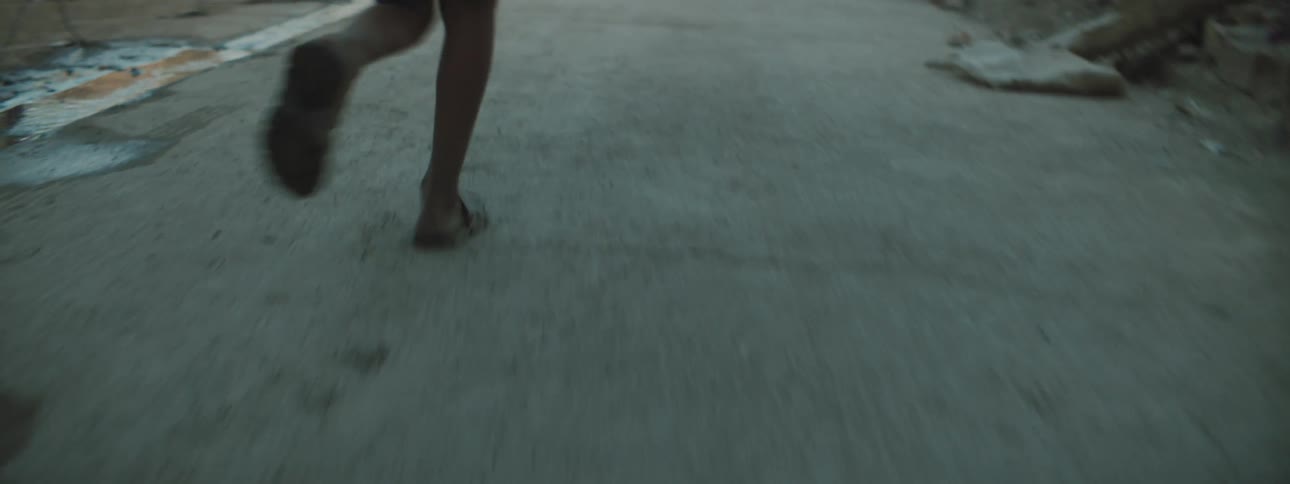 A boy runs past dilapidated buildings and rubble