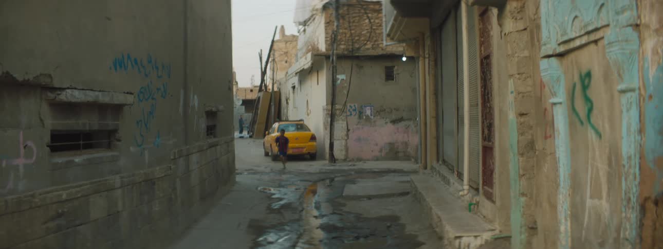 A boy runs down an urban alleyway next to a puddle on the ground