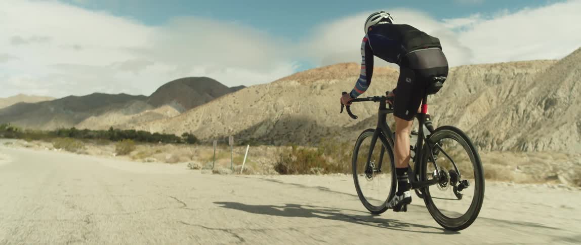 Male cyclist rides bicycle on country road with high mountains in the background
