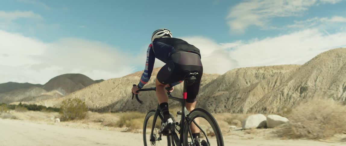 Man wearing a helmet rides a bicycle on a road in the desert close to the mountains