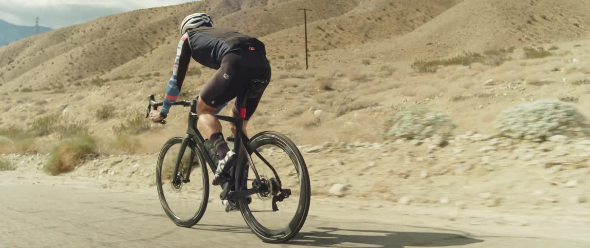 A man wearing a bicycle helmet is riding a bike on a road near mountains