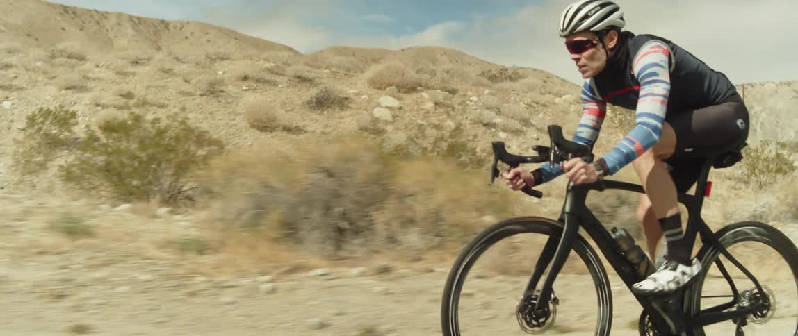 A man cycles along a road through a hilly arid countryside during the day