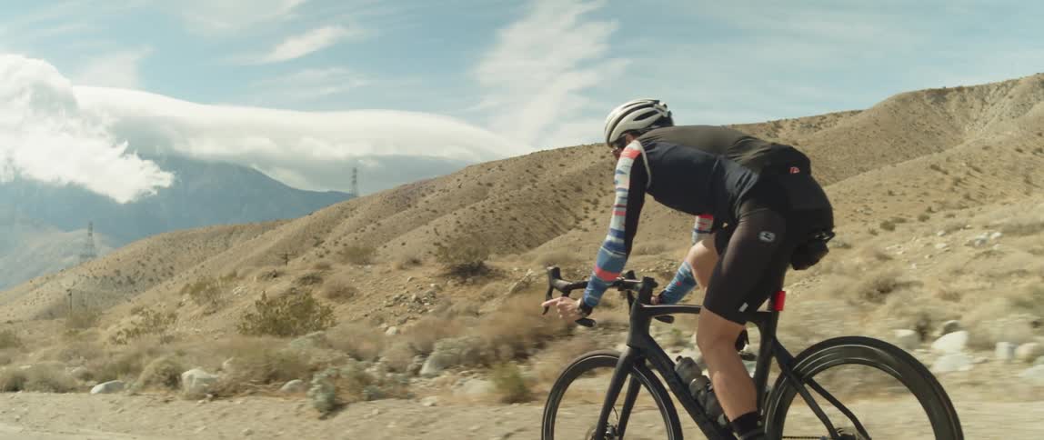 Man wearing a helmet rides a bicycle on a road in the desert close to the mountains