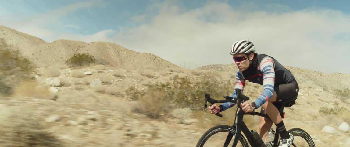 Man wearing a helmet rides a bicycle on a road in the desert close to the mountains
