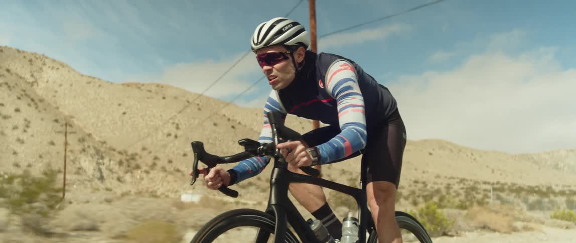 Man wearing a helmet rides a bicycle on a road in the desert close to the mountains