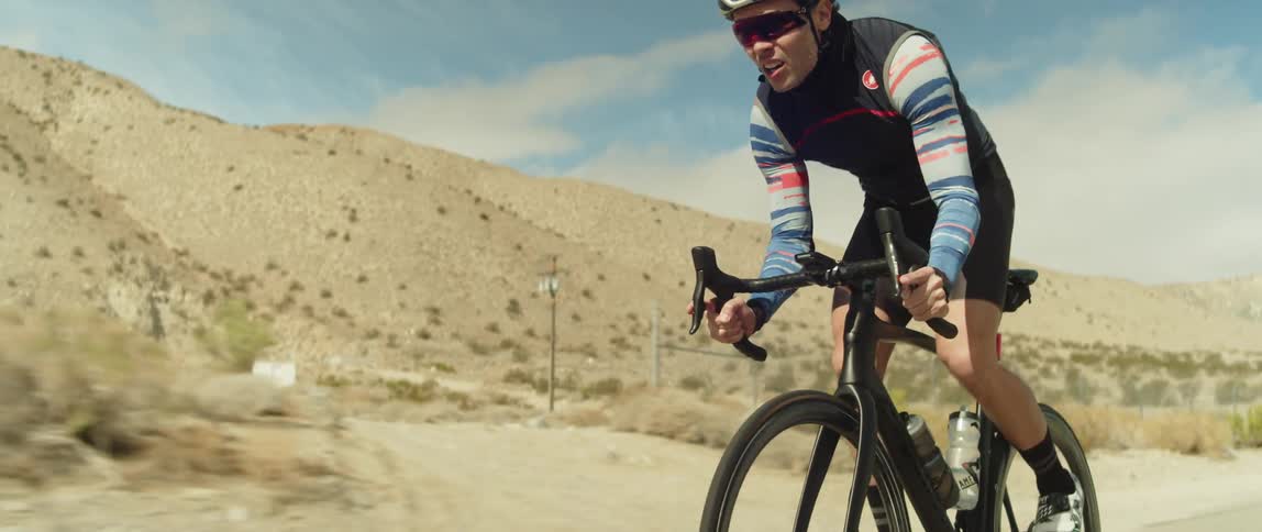 A man wearing a bicycle helmet and sunglasses is riding a bike near mountains