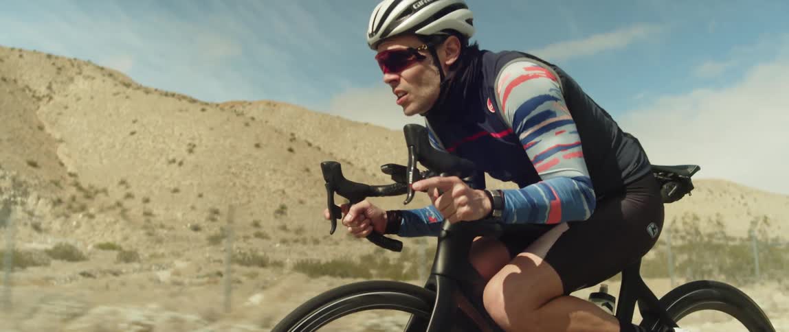 A man wearing a bicycle helmet and sunglasses is coasting on a bike near mountains