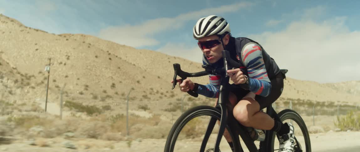 A man is riding his bicycle through a desert area
