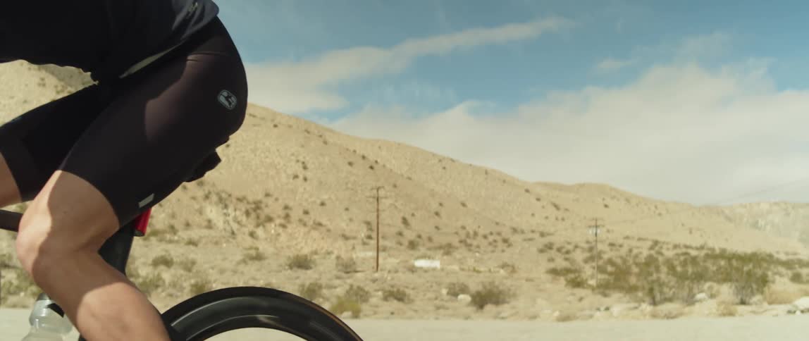 A man wearing a bicycle helmet and sunglasses is coasting on a bike near mountains