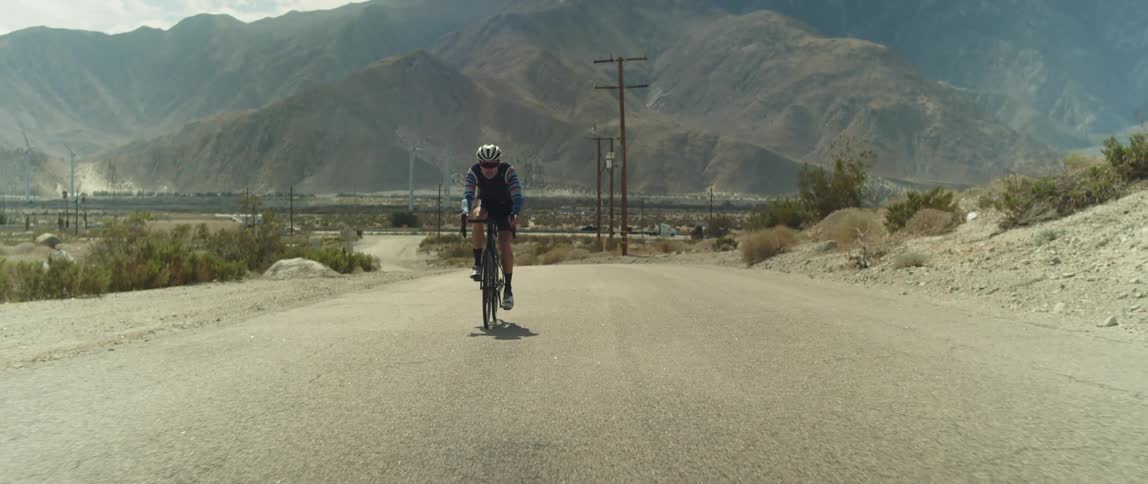 Male cyclist with helmet glasses shorts and jersey shirt cycles on country road
