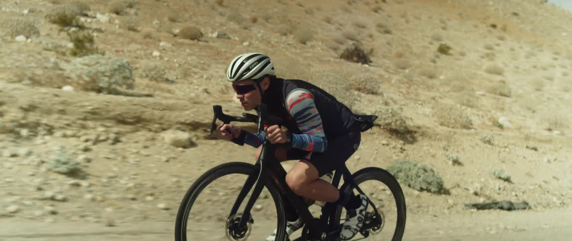 A cyclist keeps his body low as he rides a bicycle along a road through a hilly countryside during the day