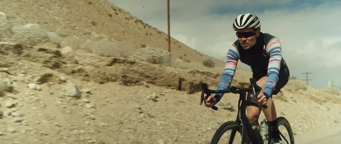A man wearing a helmet and sunglasses is riding a bike near mountains