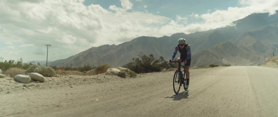 A man cycles along a road through the countryside during the day