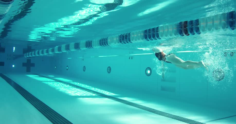 A female swimmer is seen from below the water as she swims in a pool lane