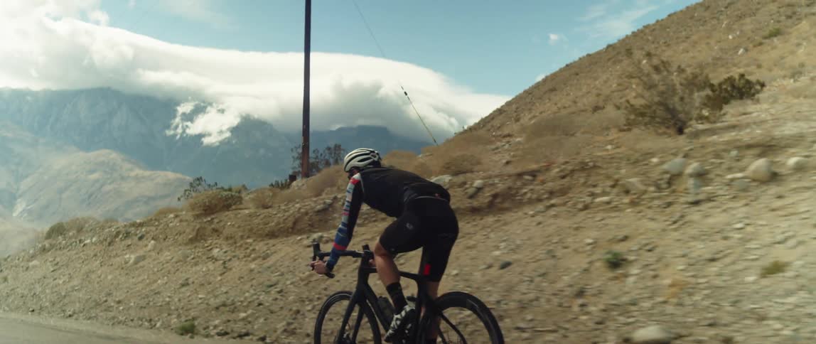Male cyclist rides bicycle on country road with high mountains in the background