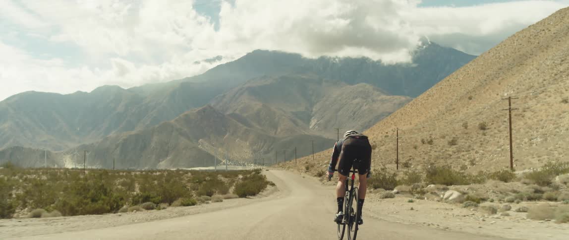 Male cyclist rides bicycle on country road with high mountains in the background