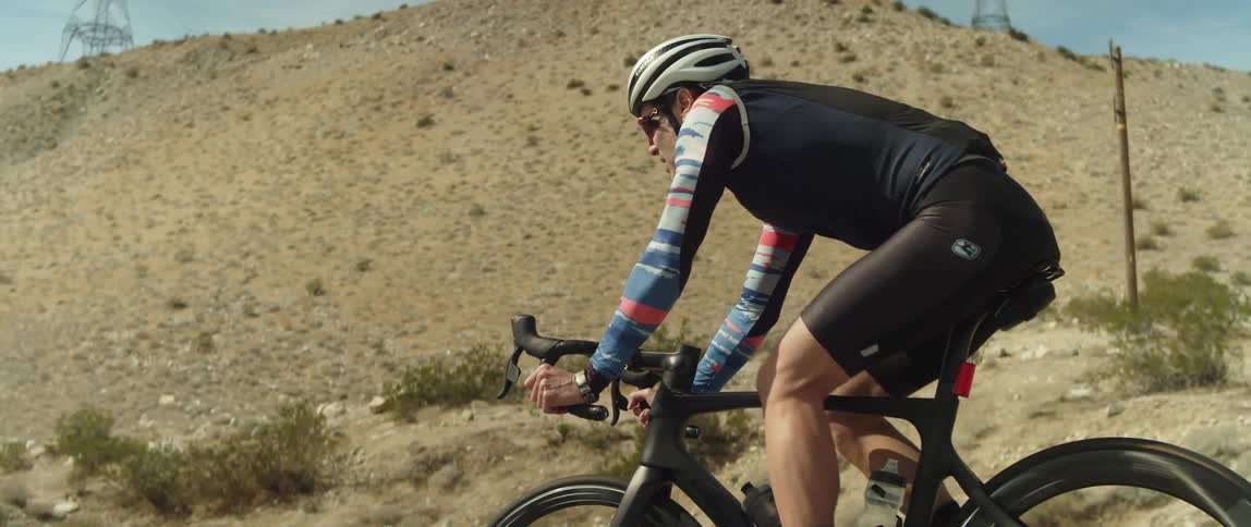 A man in a helmet riding a bicycle in a desert setting