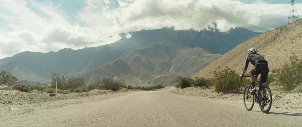 A cyclist rides a bicycle along a road through an arid countryside during the day