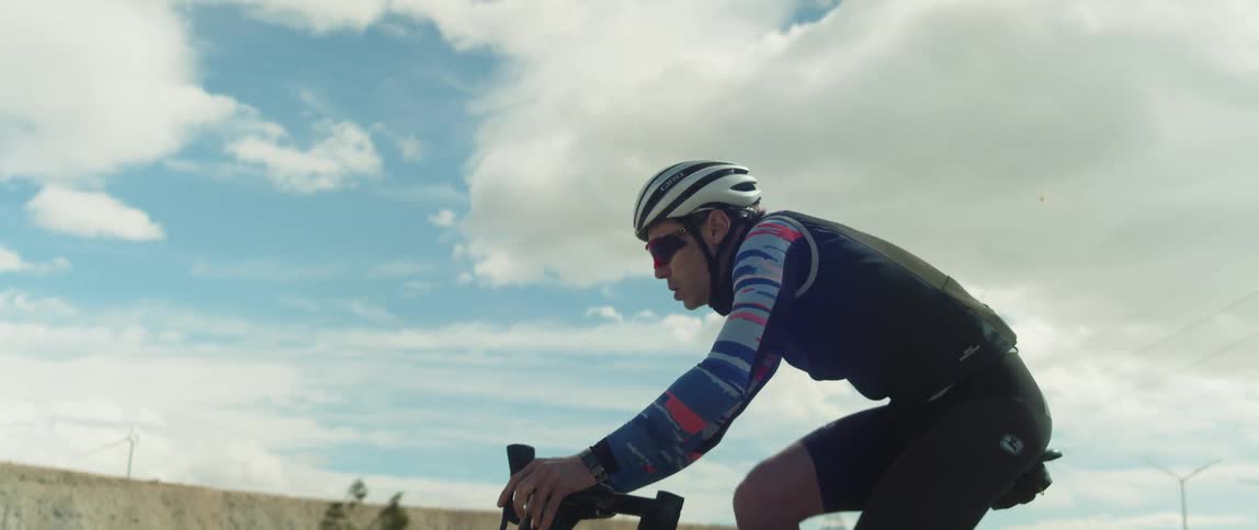 Man rides a bicycle on a desert close to wind turbines and transmission towers
