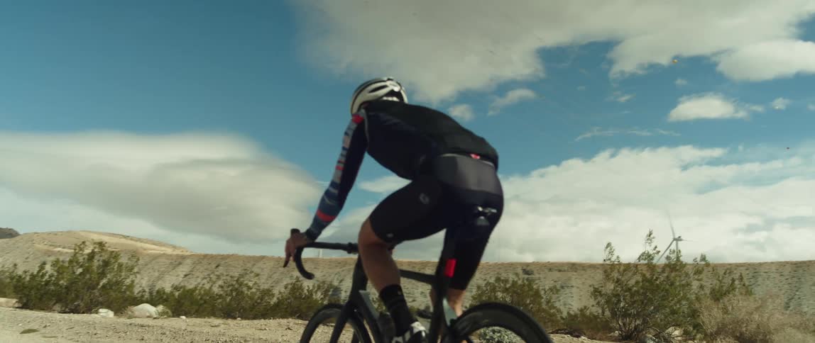 A man wearing a bicycle helmet is riding a bike on a road near mountains