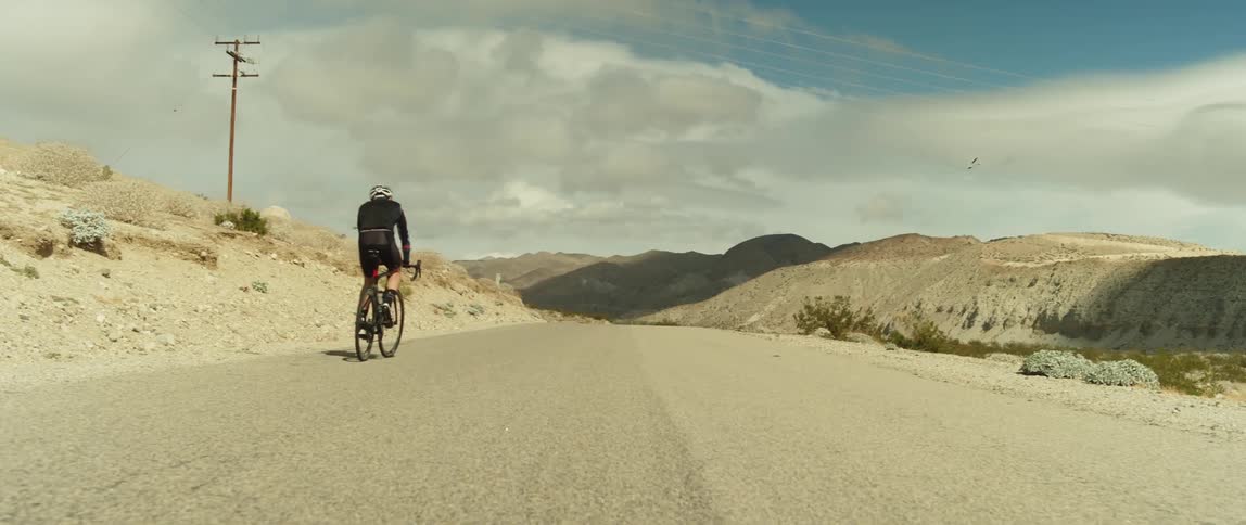 A man wearing a bicycle helmet is riding a bike a dirt road toward mountains