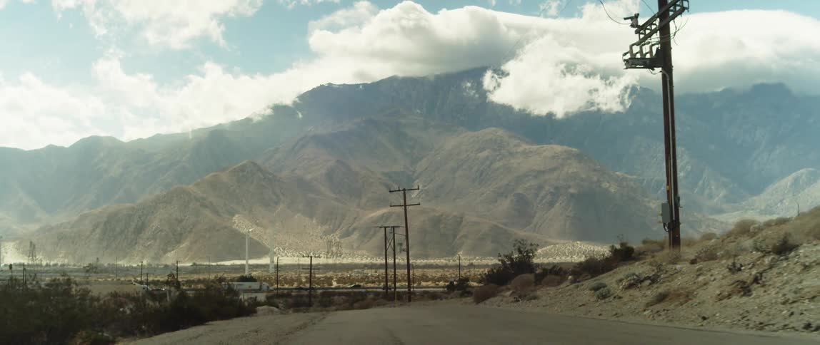 A rural dirt road with mountains and vehicles in the distance