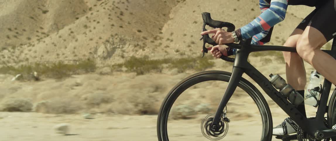 A cyclist rides a bicycle along a road through an arid countryside during the day