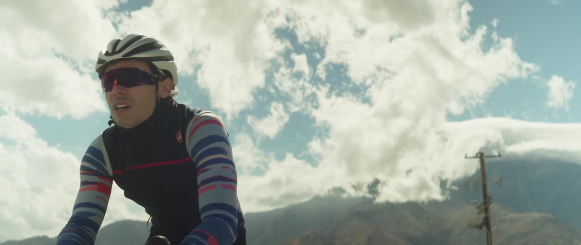Man wearing a helmet rides a bicycle on a road in the desert close to the mountains