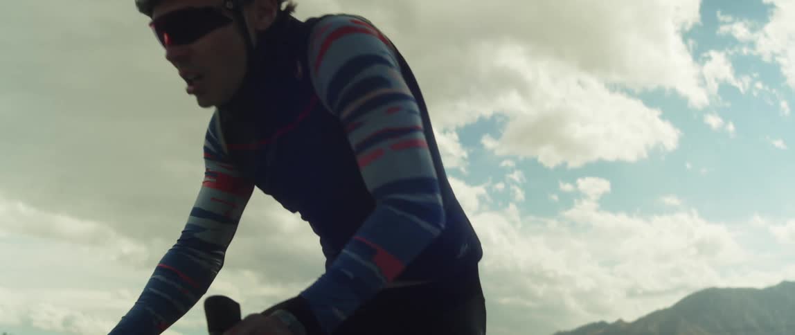 Man wearing a helmet and sunglasses rides a bicycle outdoors close to the mountains