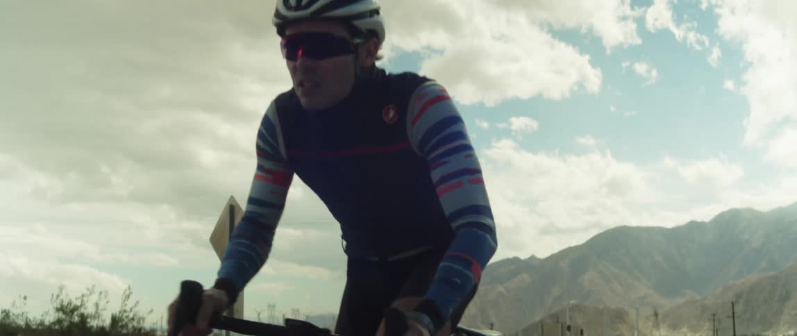A cyclist rides his bike on a roadway surrounded by mountains and rocks