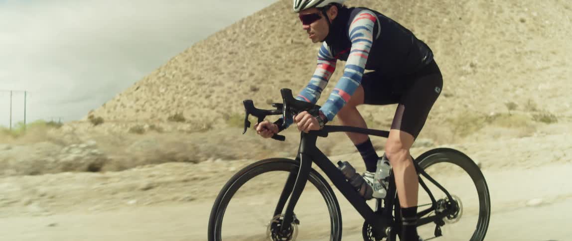 Man wearing a helmet rides a bicycle on a road in the desert close to the mountains