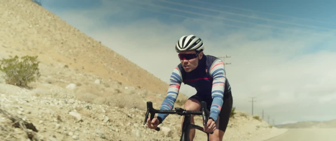 A cyclist rides a bicycle along a road through a hilly arid countryside during the day